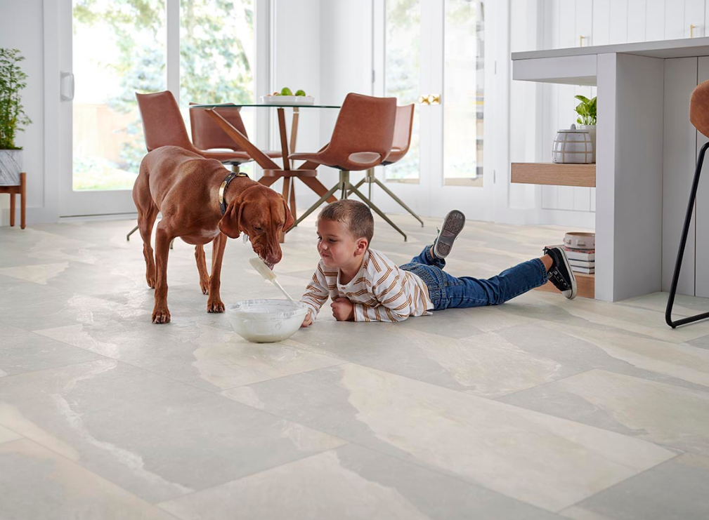 A young boy and dog make a mess on Mohawk luxury vinyl tile floors in a grey marbled pattern.
